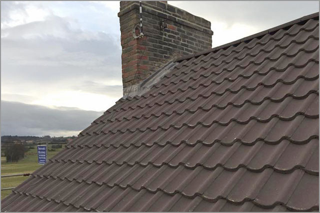 Interlocking tile roof with a re-flashed chimney stack
